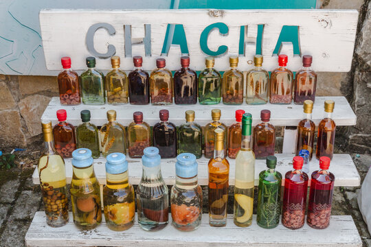 Mtskheta, Georgia - 20 August 2025: View of an array of colorful Chacha bottles displayed on a rustic wooden shelf, each holding unique infusions against a textured stone backdrop.