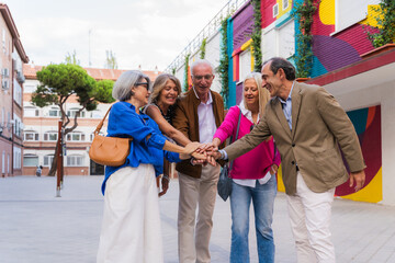 Group of happy senior friends stacking hands together outdoors celebrating friendship