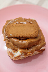 Vertical close-up of a freshly baked cinnamon roll smothered in creamy biscoff spread and topped with a whole lotus biscoff cookie on a pink plate