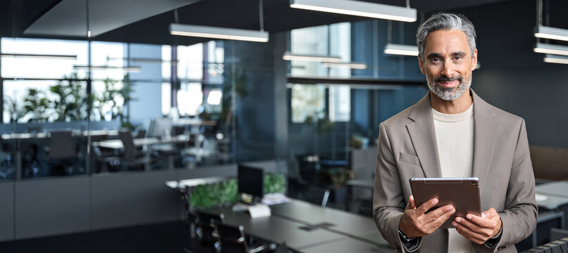 Happy confident mature business man executive standing in corporate office using digital tablet. Smiling middle aged professional businessman manager wearing suit looking at camera at work, banner. - Powered by Adobe