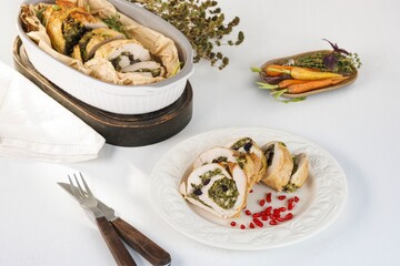 A sliced turkey roll, stuffed with greens and olives, sits on a plate. Carrots are in a tray nearby. All are ready to be enjoyed on this sunny day