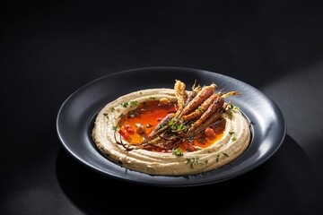 A delightful platter presents creamy hummus, artfully swirled and pooling with vibrant Chili crisp. Roasted carrots nestle atop, garnished with fresh herbs