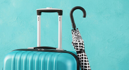 Close up of a bright turquoise blue rolling suitcase with the handle extended next to a folded black and white patterned umbrella against a teal wall