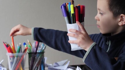 Child's Hand Reaching for Orange Pencil While Holding Cluster of Markers for Creative Project