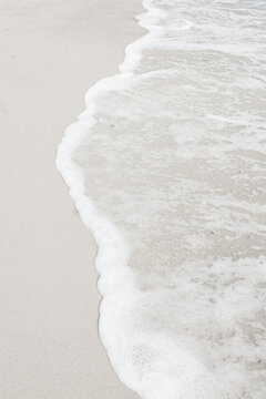 A tranquil coastal scene where smooth sand meets foamy shoreline as gentle waves roll in.Perfect for themes of relaxation, nature, vacation.Demonstrating trendy white color of 2026 year - cloud dancer