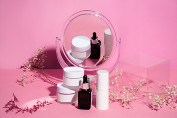 Cosmetic cream containers and mirror on pink background