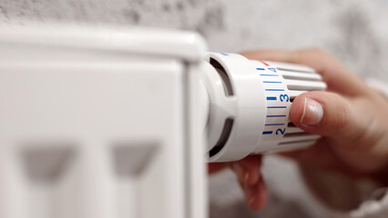 Hand adjusting a white radiator thermostat dial, demonstrating temperature control in a cozy indoor environment, highlighting home comfort and energy efficiency