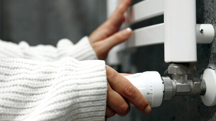 Person adjusting a radiator valve with a white sweater on, demonstrating home heating maintenance...