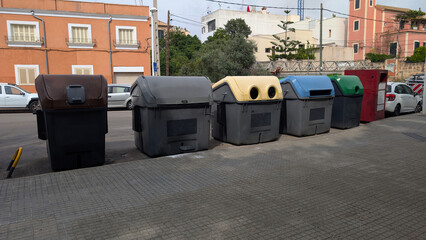 Row of public recycling and waste containers on paved city sidewalk in Son Espanyolet neighborhood of Palma de Mallorca. Urban waste management infrastructure, dumpster, trash bin, garbage, refuse.