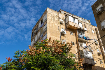 Weathered Israeli residential building with balconies laundry shutters and external AC units under blue sky. Aged stucco facade and urban neighborhood housing