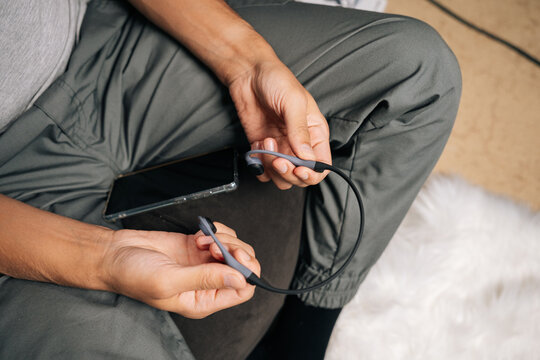 Top view of male hands holding bone-conduction headphones next to smartphone, showcasing ear-free wireless audio tech for music, podcasts and calls while staying aware of surroundings.