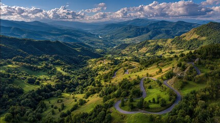 Aerial View Of Lush Green Mountainous Landscape With Winding Road Under A Blue Sky With Clouds