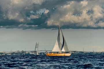 Obraz premium The lonely old wooden sailboat at sunny day, bridge on background, sailing regatta in the Gulf of Finland, sailing yacht competing in a race, splashing water, board the boat