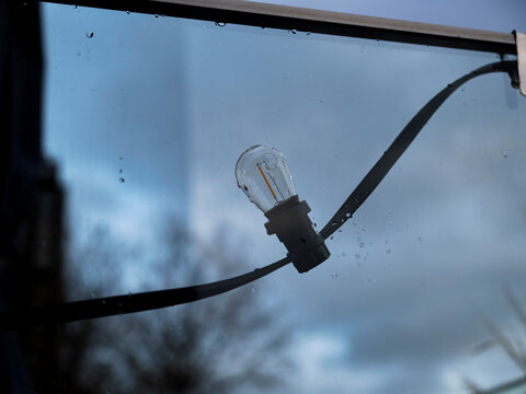 Edison-style vintage light bulb with rain droplets on glass against soft blue rainy background. - Powered by Adobe