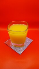 A glass of freshly squeezed orange juice on a sparkling coaster with a red background 