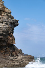 massive layered rock cliff at Las Catedrales Beach in Spain, a wave crashes powerfully at the base, contrasting the dynamic ocean with the ancient geological strata