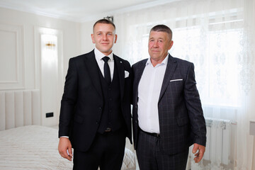 Men dressed in formal attire stand together in a bright room before a celebration event