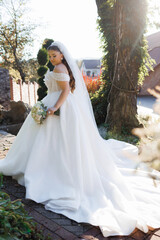 Elegant bride in white gown holding bouquet outdoors on sunny day