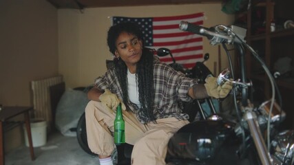 Relaxing in a garage after working on a motorcycle while enjoying a drink with an American flag in the background