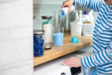 Female housewife hands sprinkle dry blue granular laundry conditioner glass can storage organizing
