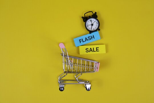 A miniature shopping cart sits on a yellow backdrop beside a small clock and colorful signs reading 'Flash' and 'Sale', conveying urgency, discounts, and quick shopping ideas. - Powered by Adobe