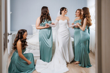 Bridesmaids help the bride get ready for her wedding day in a bright room