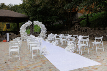 Outdoor wedding ceremony setup with white chairs and floral arch in a serene garden