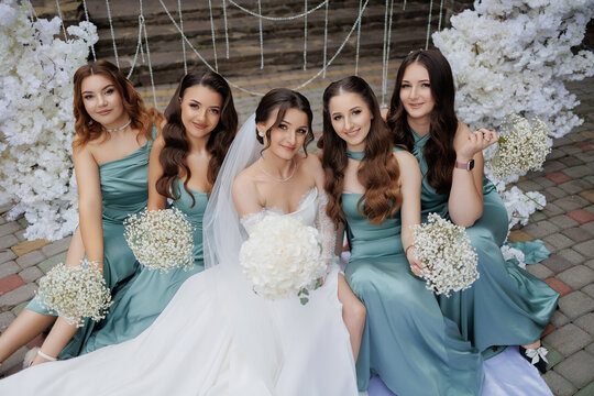 Bride poses with bridesmaids in green dresses holding flower bouquets at outdoor wedding - Powered by Adobe