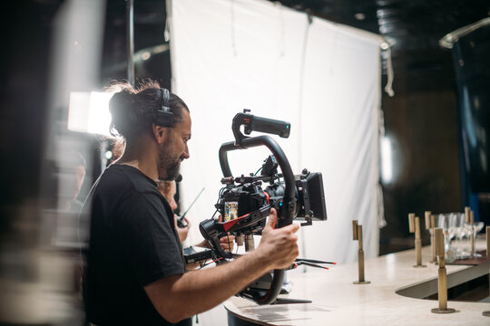 Director of photography with a camera in his hands on the set. Professional videographer at work on filming a movie, commercial or TV series. Filming process indoors, studio