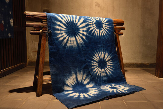 A traditional "adire" (tie-dye fabric), with vibrant indigo patterns, draped elegantly on a simple wooden display stand.