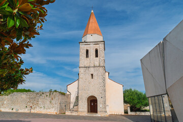 Historic stone church with orange steeple and blue sky in peaceful courtyard setting. Church of the Mother of God Health. Town of Krk, Krk island, Croatia