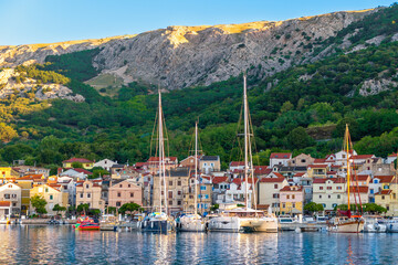 Quaint coastal village with sailboats and scenic mountain backdrop at sunset. Baška, Krk island, Croatia