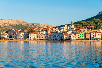 Fototapeta premium Scenic coastal town with colorful buildings and mountains at sunset. Baška, Krk island, Croatia