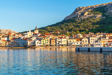 Fototapeta premium Coastal townscape at sunset with mountainous backdrop and calm waters. Baška, Krk island, Croatia