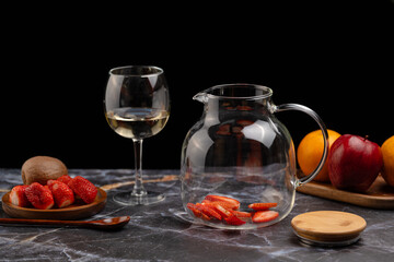 Glass pitcher with sliced ​​strawberries and a wine glass in the background, preparing sangria