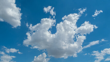 Bright blue sky filled with a large, dramatic cumulus cloud formation and scattered smaller clouds on a clear, sunny day