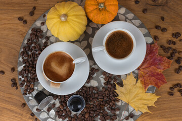 Autumn coffee scene with two cups, coffee beans, pods, colorful leaves and pumpkins on wooden table