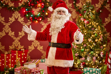 Santa Claus in traditional red suit welcomes guests with decorated Christmas trees and wrapped presents