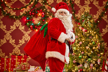 Santa Claus carrying gift sack in front of decorated Christmas tree with twinkling lights