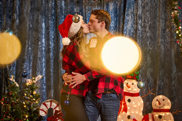 Couple shares a romantic kiss surrounded by festive Christmas decorations and twinkling lights