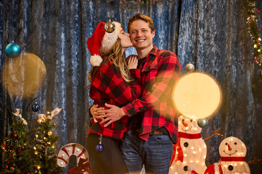 Couple in matching plaid shirts celebrating Christmas with festive decorations and holiday photo booth backdrop