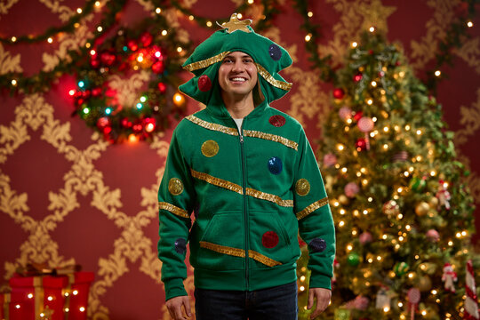 Man wearing festive green Christmas tree hoodie with ornaments and gold tinsel trim