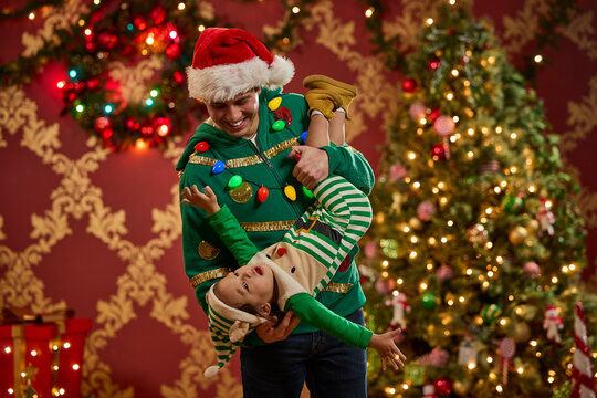 Father and son wearing festive ugly Christmas sweaters celebrate the holidays together at home