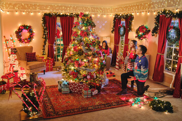Family enjoying festive holiday living room decorated with illuminated Christmas tree, wreaths, and twinkling lights