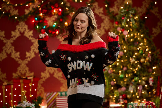 Woman wearing festive black and red ugly Christmas sweater with snow design and decorative embellishments