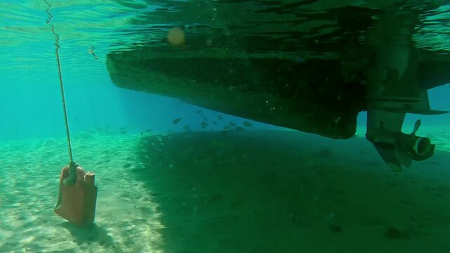 Fishing boat moored above a sandy seabed, a school of fish hiding in its shadow on a bright sunny day, Slow motion