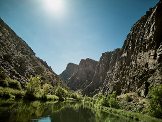 Scenic river canyon with towering rock cliffs and lush green vegetation under blue sky
