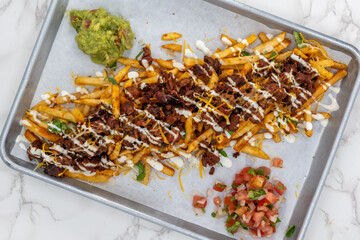 Overhead view of Latino food for a hungry patron includes a huge plate of asade fries loaded with cheese and sour cream