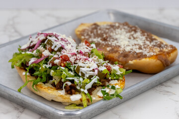 Latino food for a hungry patron includes a huge torta split in halves and loaded with meat and cheese