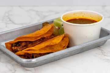 Latino food for a hungry patron includes a pair of birria tacos and consome sauce for dipping